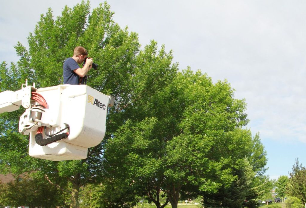 A photographer for 3RM on location in Iowa, elevated in a bucket truck attachment, using a camera to capture images